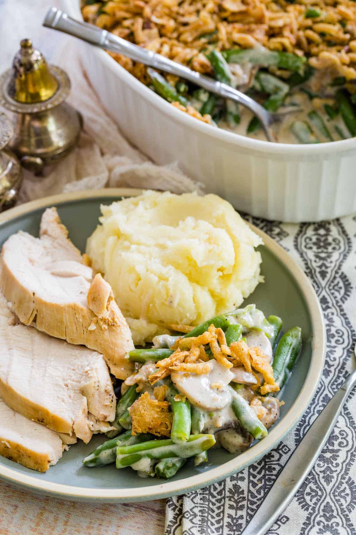 A serving of gluten-free green bean casserole on a plate next to mashed potatoes and slices of turkey.