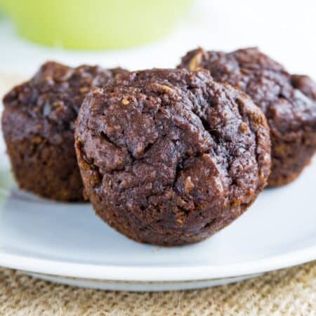 Three little chocolate pumpkin mini muffins on a small white plate.