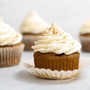 A pumpkin cupcake with cream cheese frosting sitting on top of its opened wrapper
