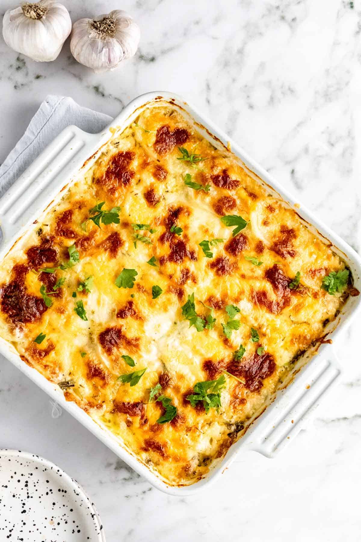 Overhead view of scalloped potatoes in a white baking dish garnished with fresh parsley.