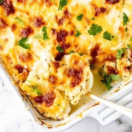 The corner of a baking dish filled with scalloped potatoes, with a serving spoon.