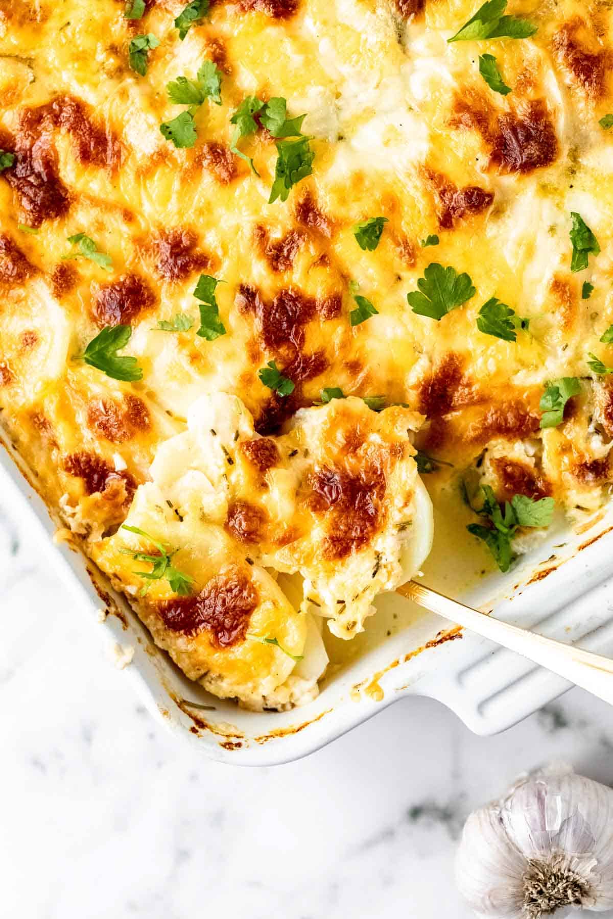 The corner of a baking dish filled with scalloped potatoes, with a serving spoon.