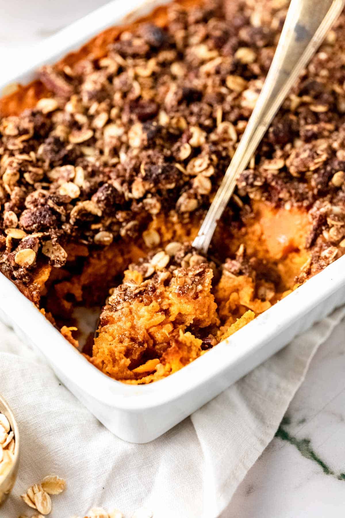 Overhead view of sweet potato casserole in a baking dish with a large serving spoon.