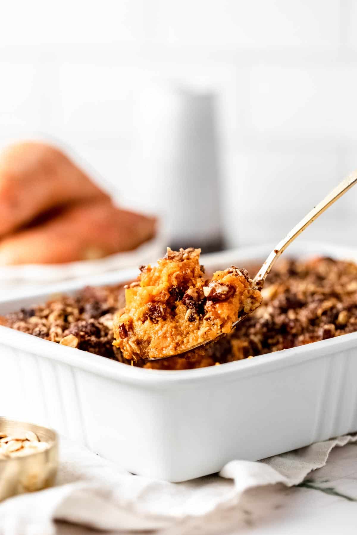 A spoon lifts a serving of sweet potato casserole from a white baking dish.