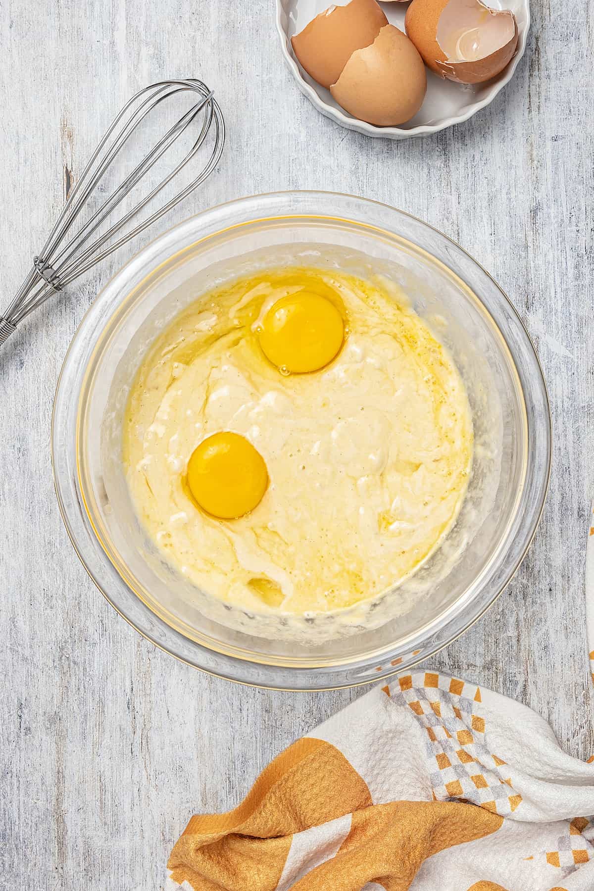 Pudding batter ingredients combined in a glass mixing bowl, next to a whisk.