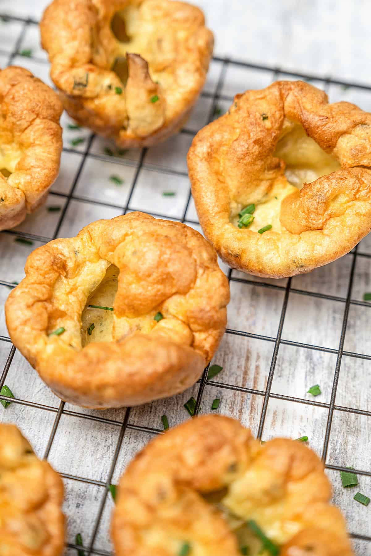 Assorted gluten-free Yorkshire pudding on a black wire cooling rack.