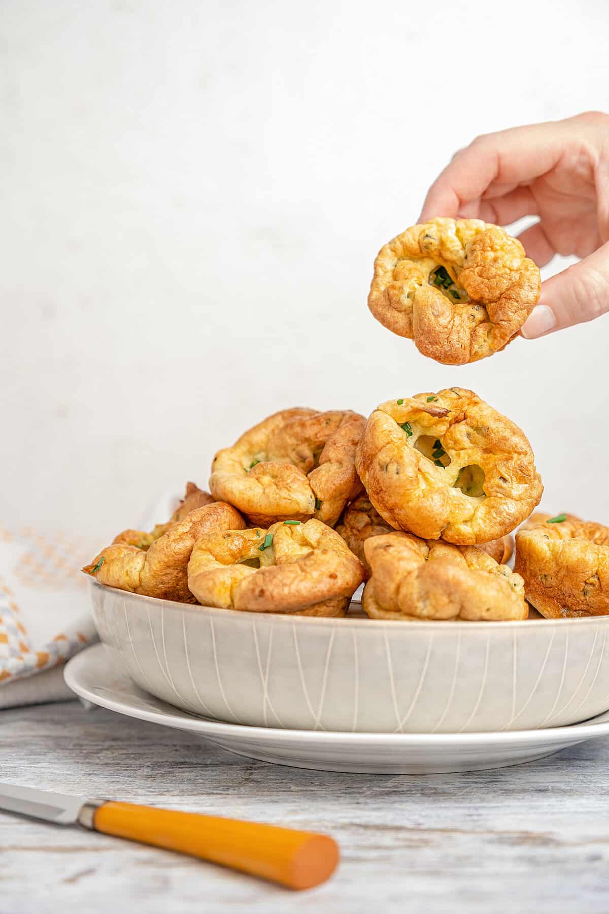 A hand lifts a gluten-free Yorkshire pudding from the top of a pile in a large bowl.