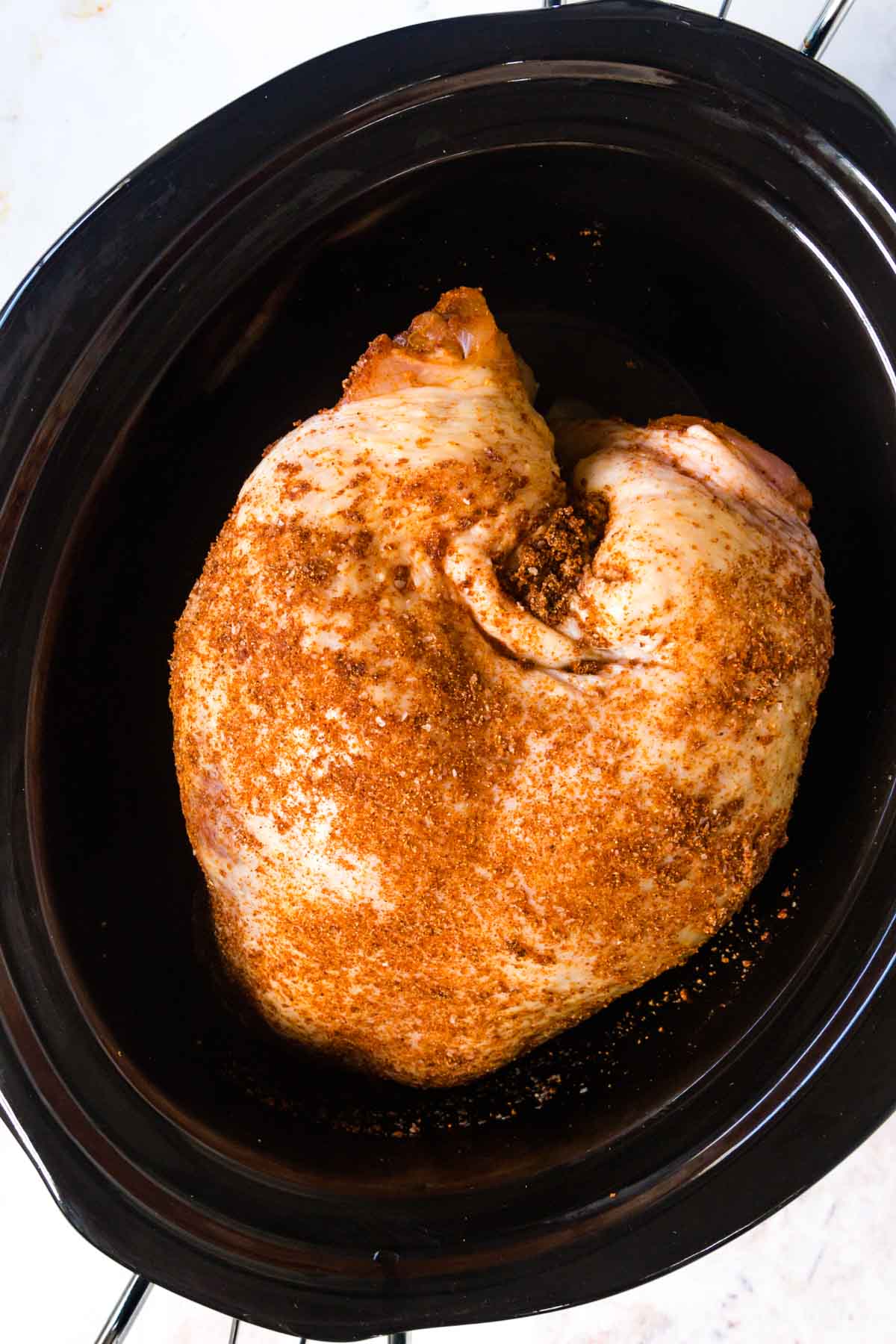 An open Crock Pot with a seasoned turkey breast at the bottom.