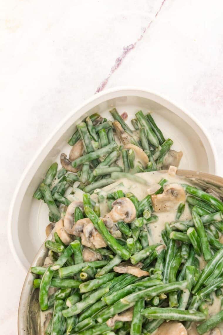 Green beans and mushroom sauce are poured into a large white baking dish.