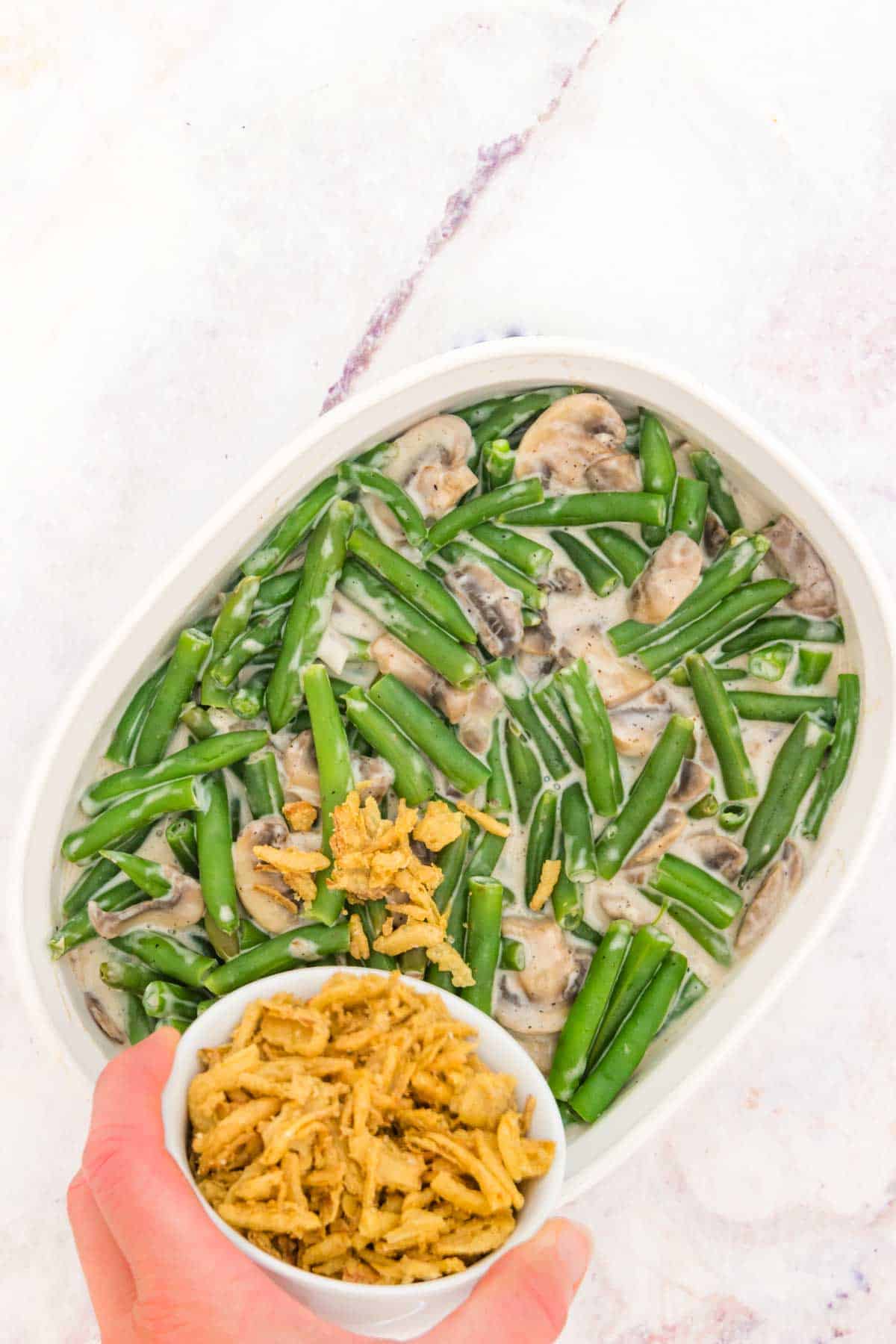 French fried onions are sprinkled over green bean casserole in a baking dish.