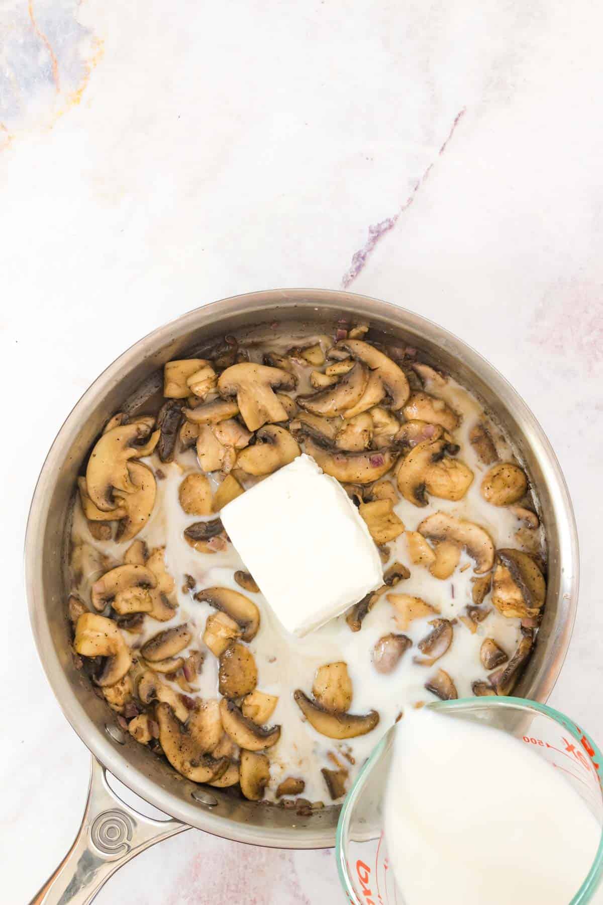 Cream cheese and milk are added into a skillet with mushrooms and onions.