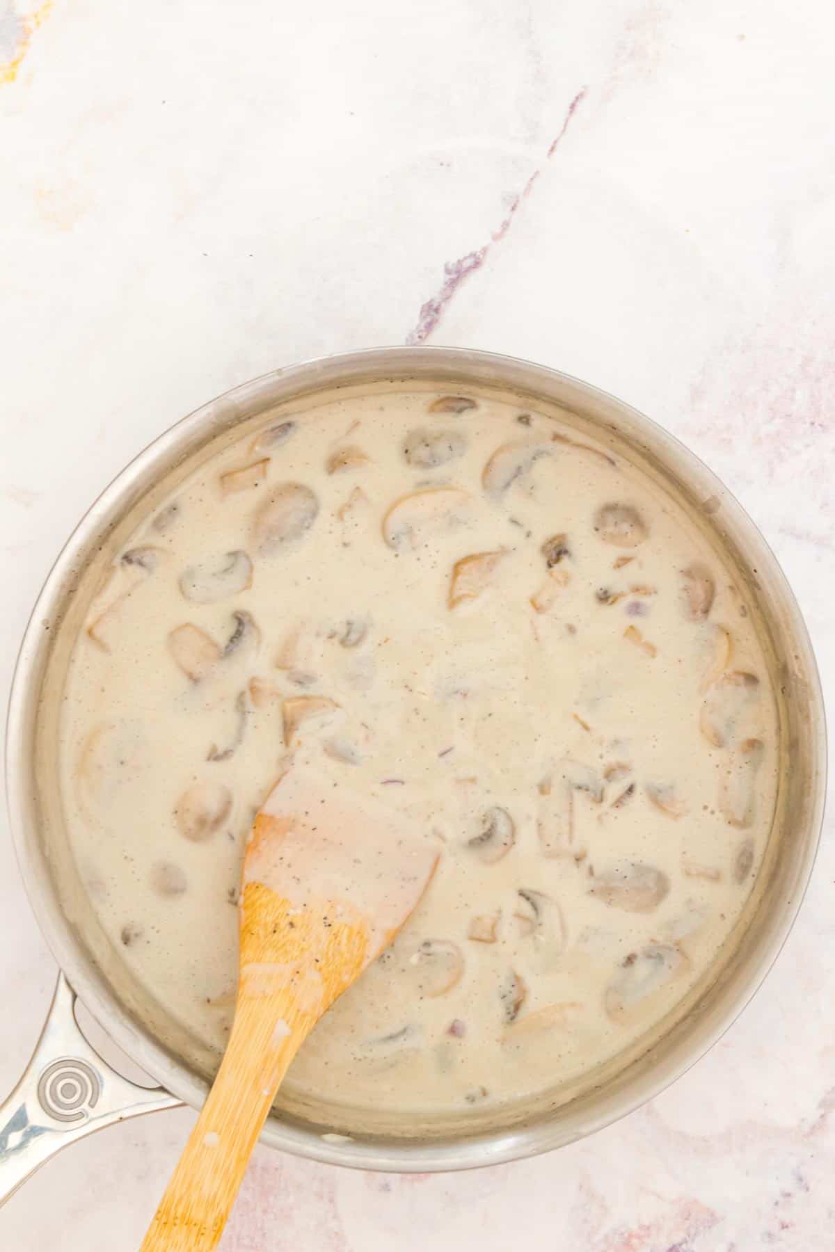 Mushroom cream sauce in a skillet with a wooden spatula.