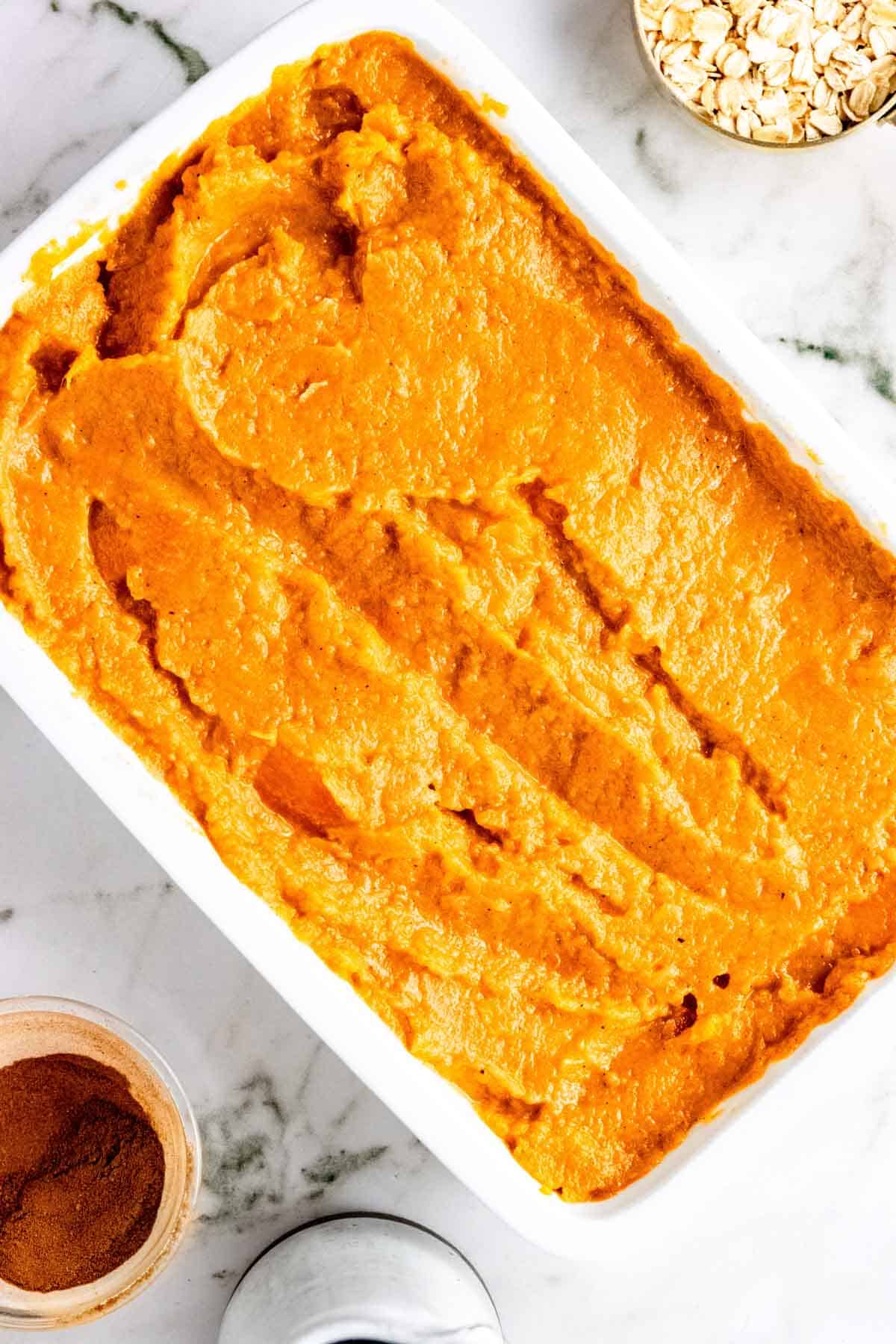 Overhead view of mashed sweet potatoes spread evenly in a large rectangular baking dish.