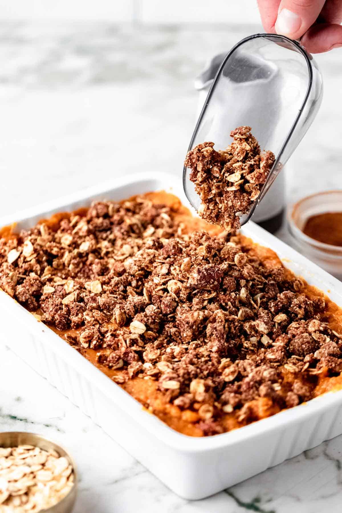 The oat topping is poured over top of a sweet potato casserole in a baking dish.