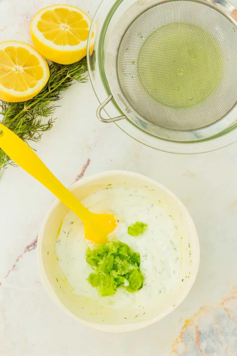 Shredded cucumber added to the yogurt tzatziki base in a bowl.