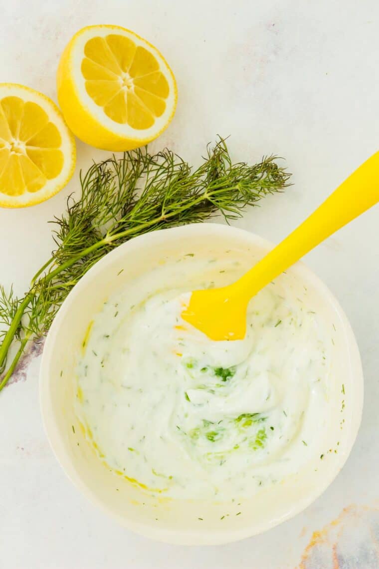 Tzatziki sauce being stirred together in a bowl with a yellow spatula.