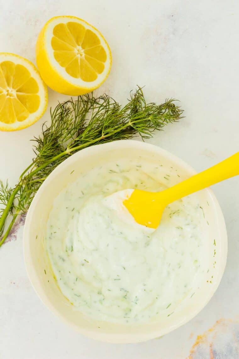 The mixed tzatziki in a bowl with lemon halves and a sprig of dill next to it.