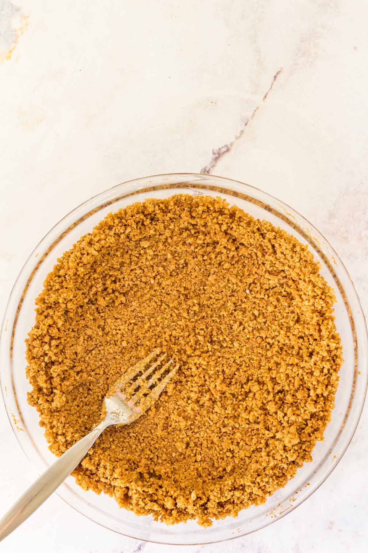 A fork is used to press graham cracker crust into a glass pie plate.