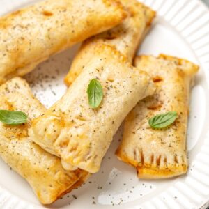 golden brown pizza pockets piled on a plate and garnished with basil leaves.
