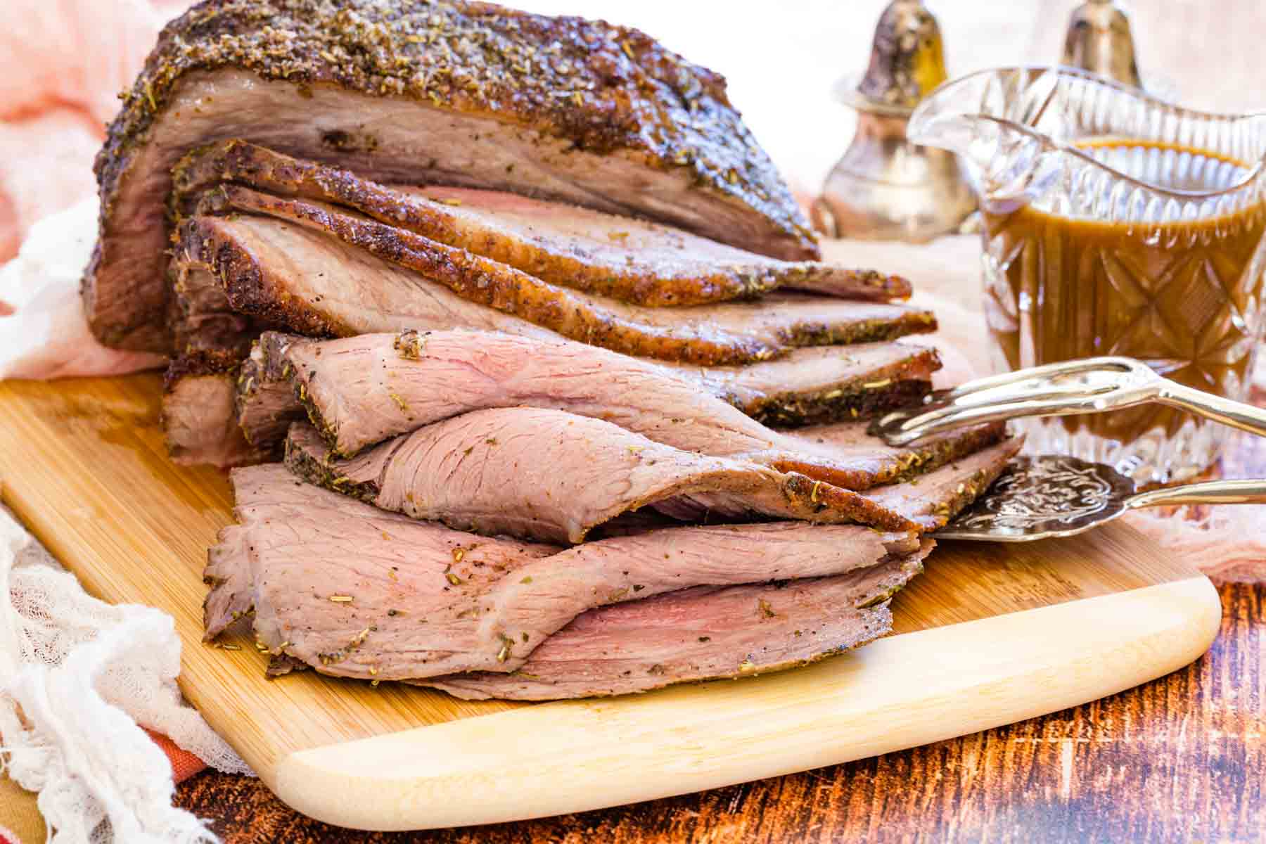 Cooked bottom round roast sliced up on a wooden cutting board.