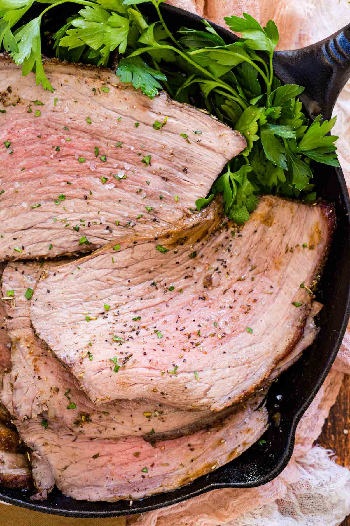 Overhead view of bottom round roast slices with fresh parsley in a cast iron skillet.