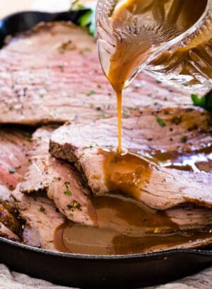Gravy is poured over slices of roast beef in a skillet.