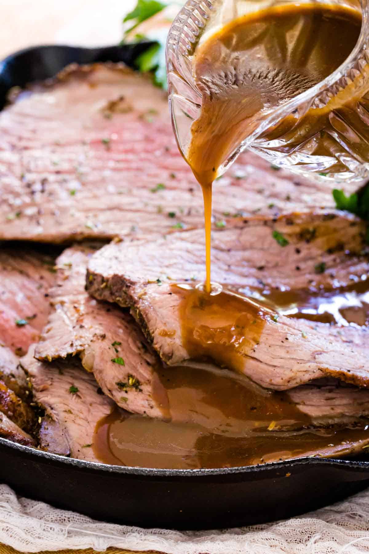 Gravy is poured over slices of roast beef in a skillet.