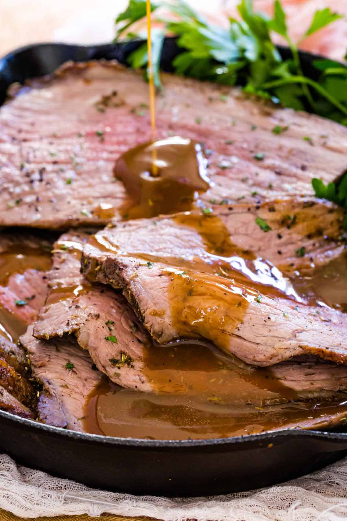 Gravy is poured over slices of roast beef in a skillet.