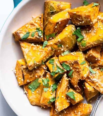 Oven Roasted Kabocha Squash with Peanut Sauce in a dish garnished with sesame seeds and herbs.