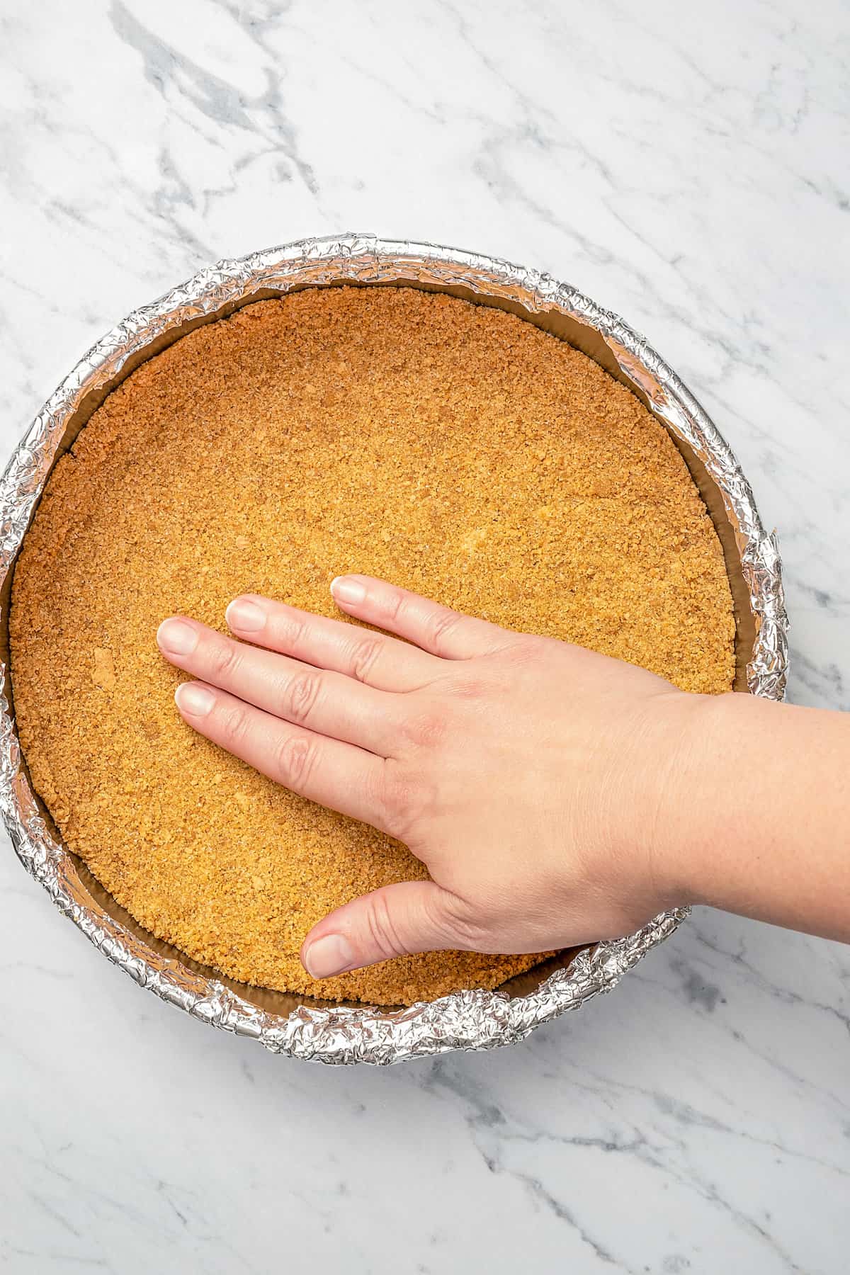 A hand pressing the Graham cracker crust into the bottom of a springform pan.