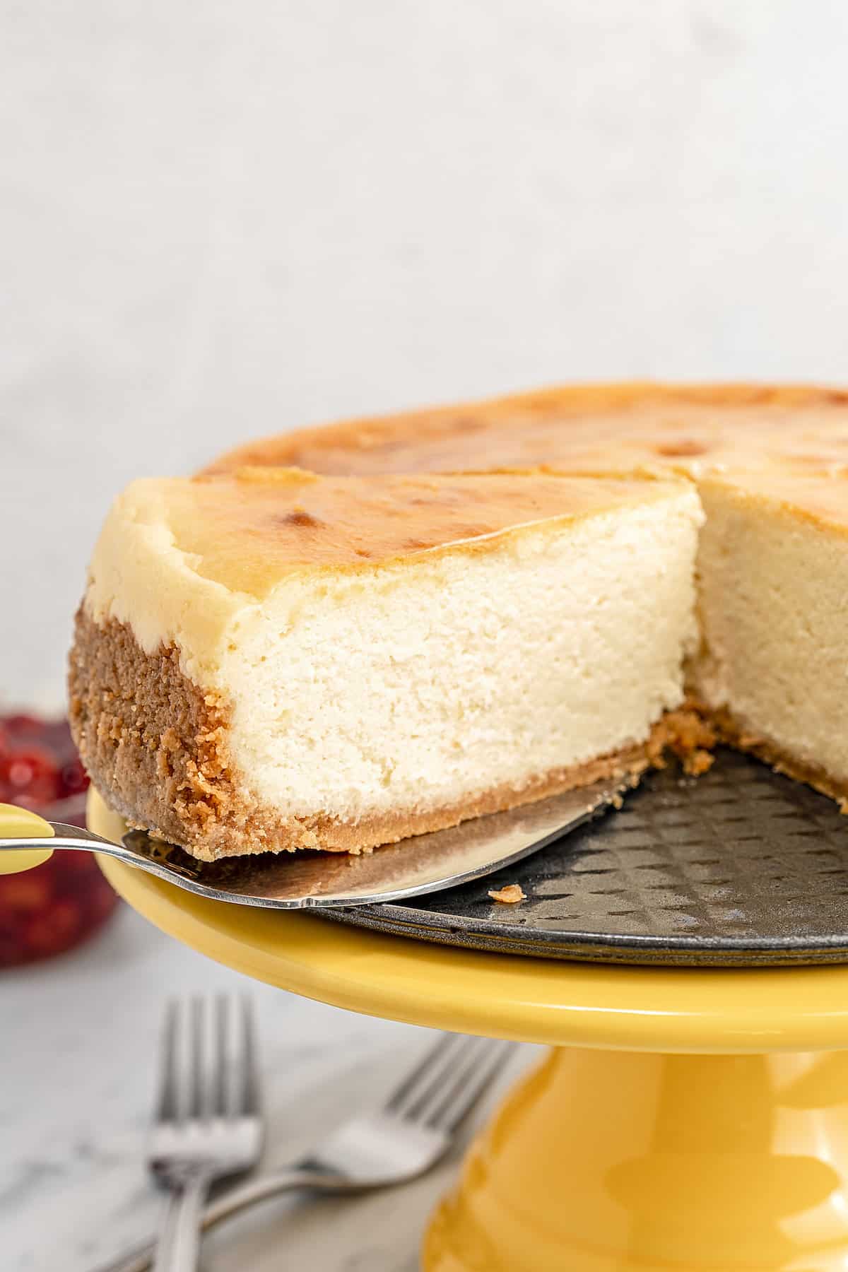 Close up of gluten-free cheesecake on a yellow cake stand with a slice missing.