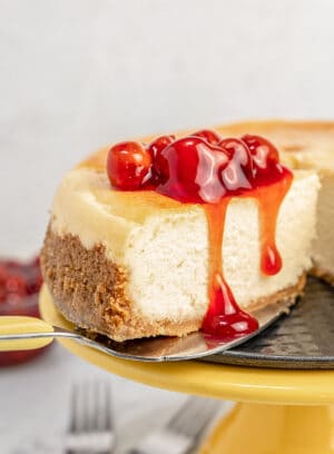 Close up of gluten-free cheesecake on a yellow cake stand topped with cherries.