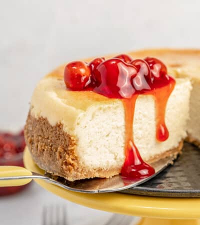 Close up of gluten-free cheesecake on a yellow cake stand topped with cherries.