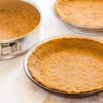 Two gluten free graham cracker crusts in glass pie plates and one in a springform pan.