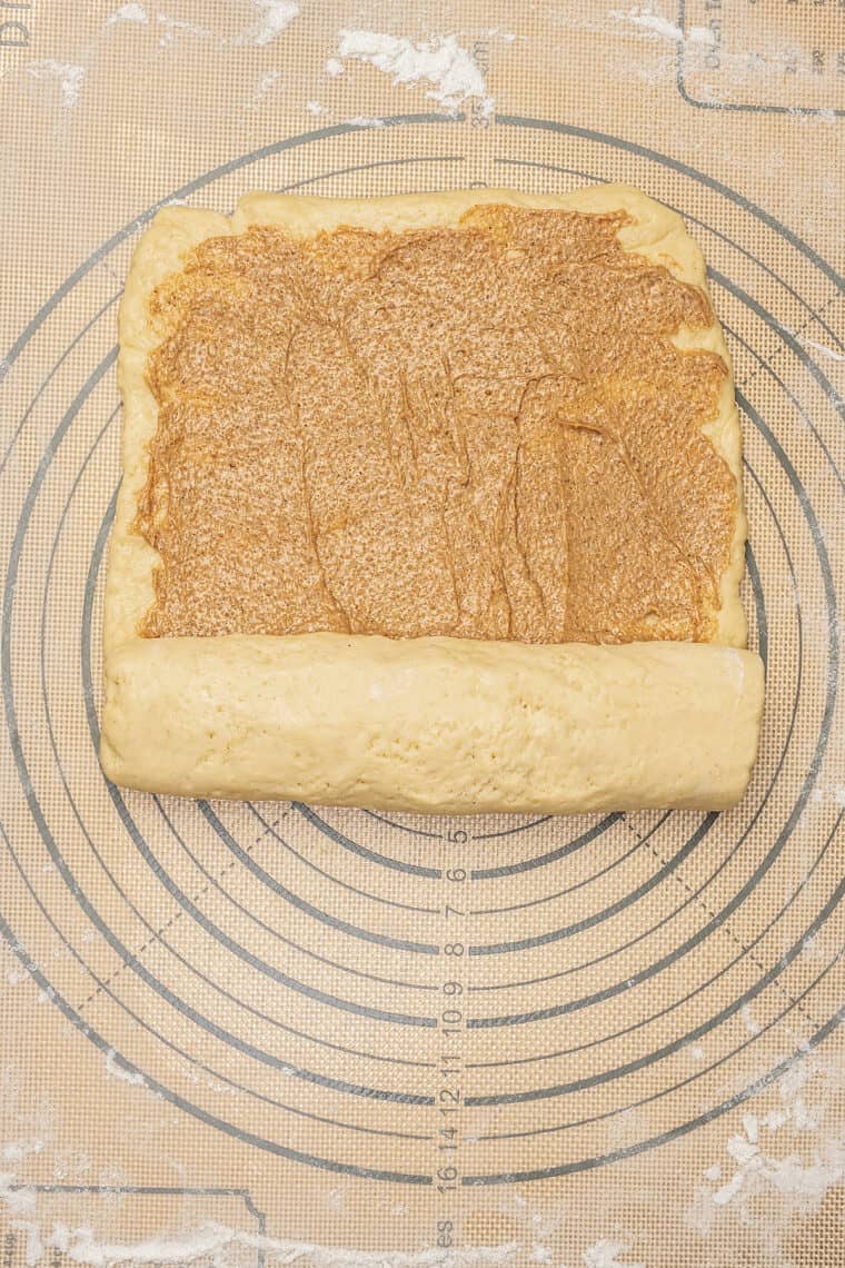 Dough filled with cinnamon butter is rolled up into a log.