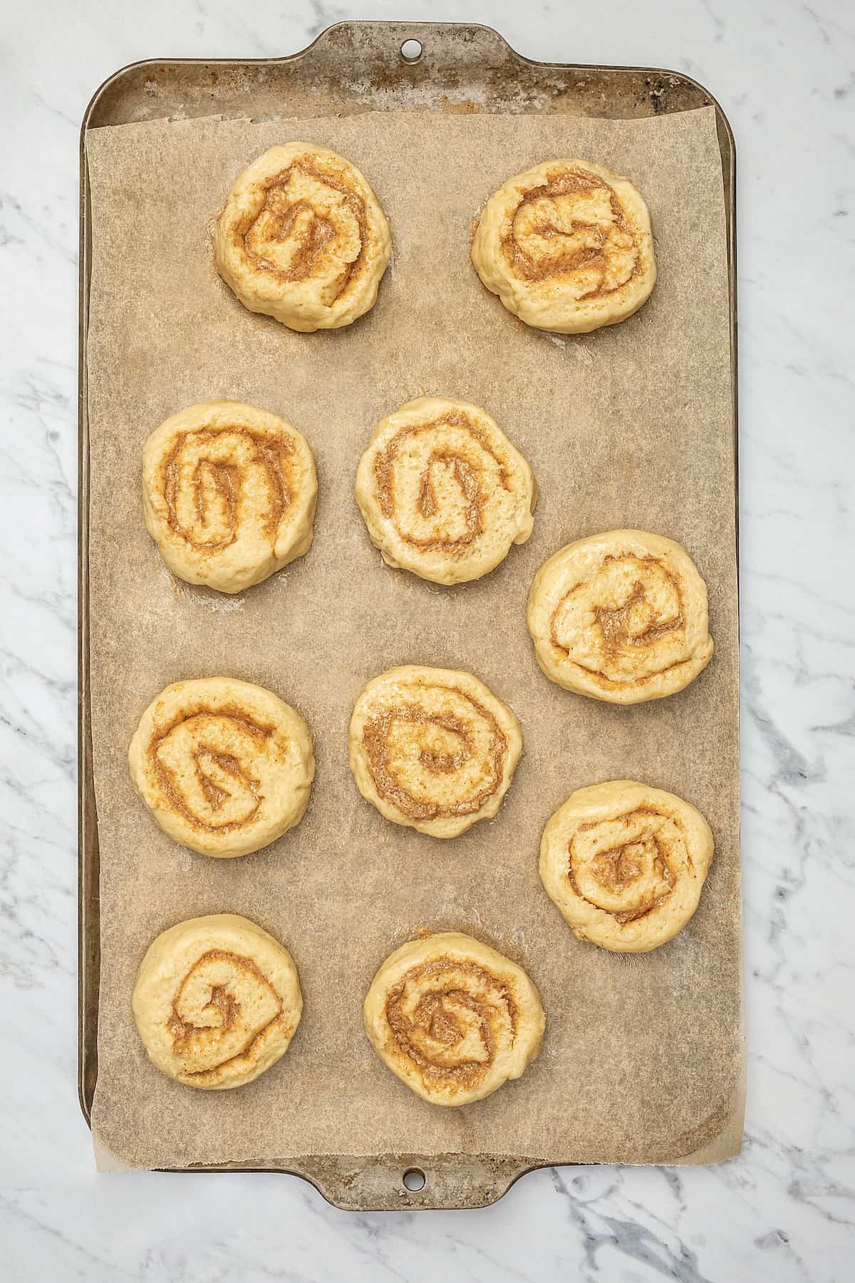 Unbaked gluten-free honey buns laid out on a baking sheet.