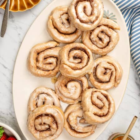 Overhead view of assorted glazed gluten-free honey buns on a large oval platter.