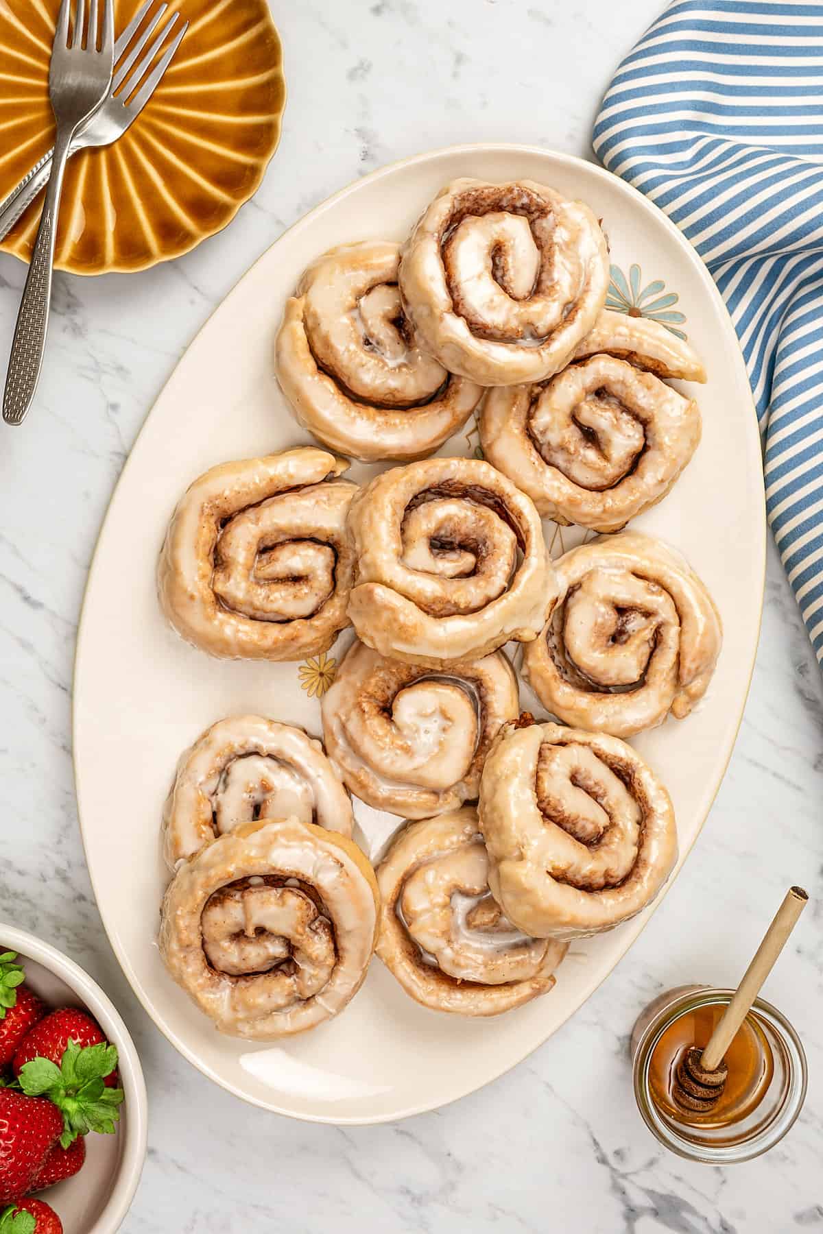 Overhead view of assorted glazed gluten-free honey buns on a large oval platter.