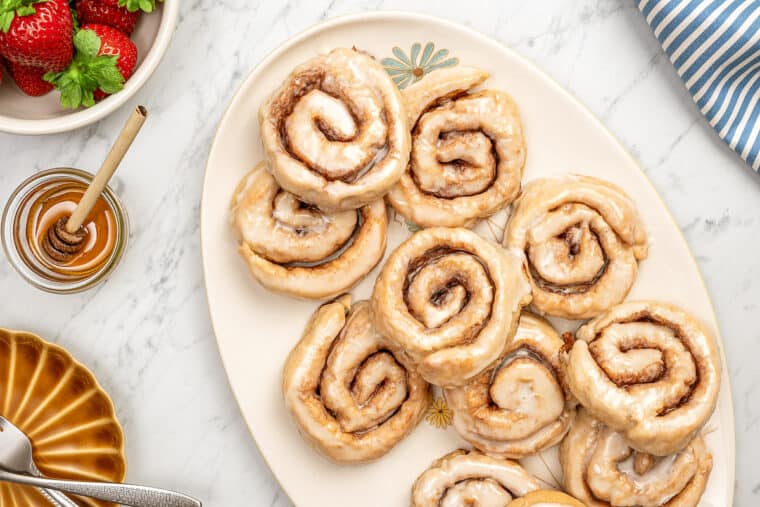 Assorted glazed gluten-free honey buns on a large oval platter.