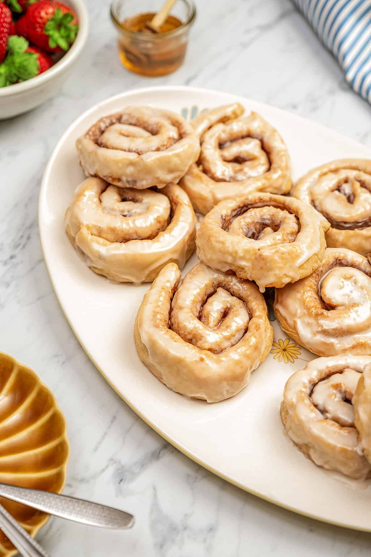 Assorted glazed gluten-free honey buns on a large oval platter.