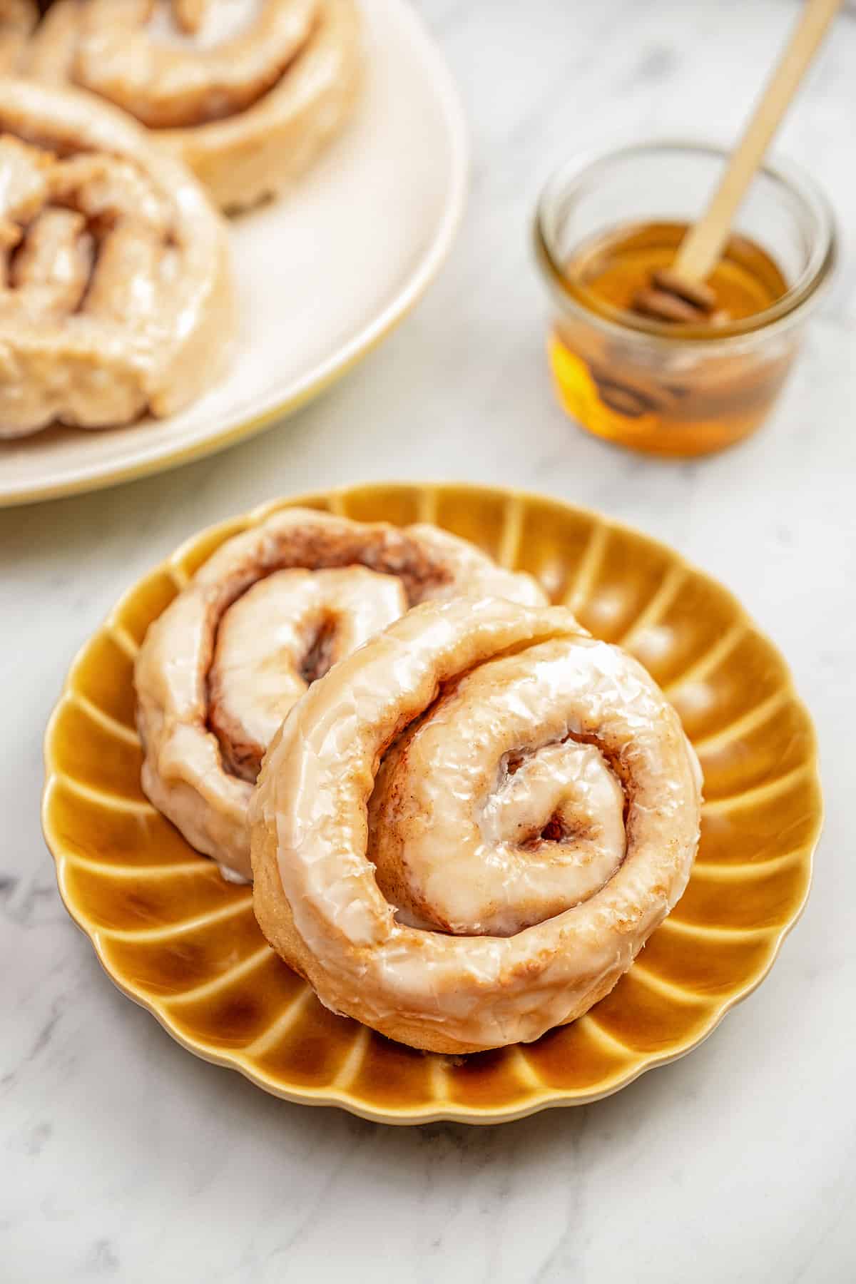 Two gluten-free honey buns on a brown plate next to a plate of honey buns.