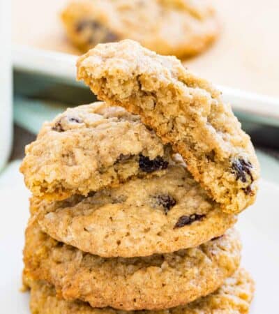 Gluten free oatmeal raisin cookies stacked on a plate, with more cookies on a baking sheet in the background.