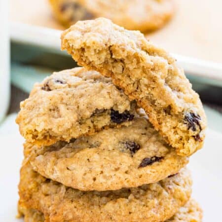 Gluten free oatmeal raisin cookies stacked on a plate, with more cookies on a baking sheet in the background.