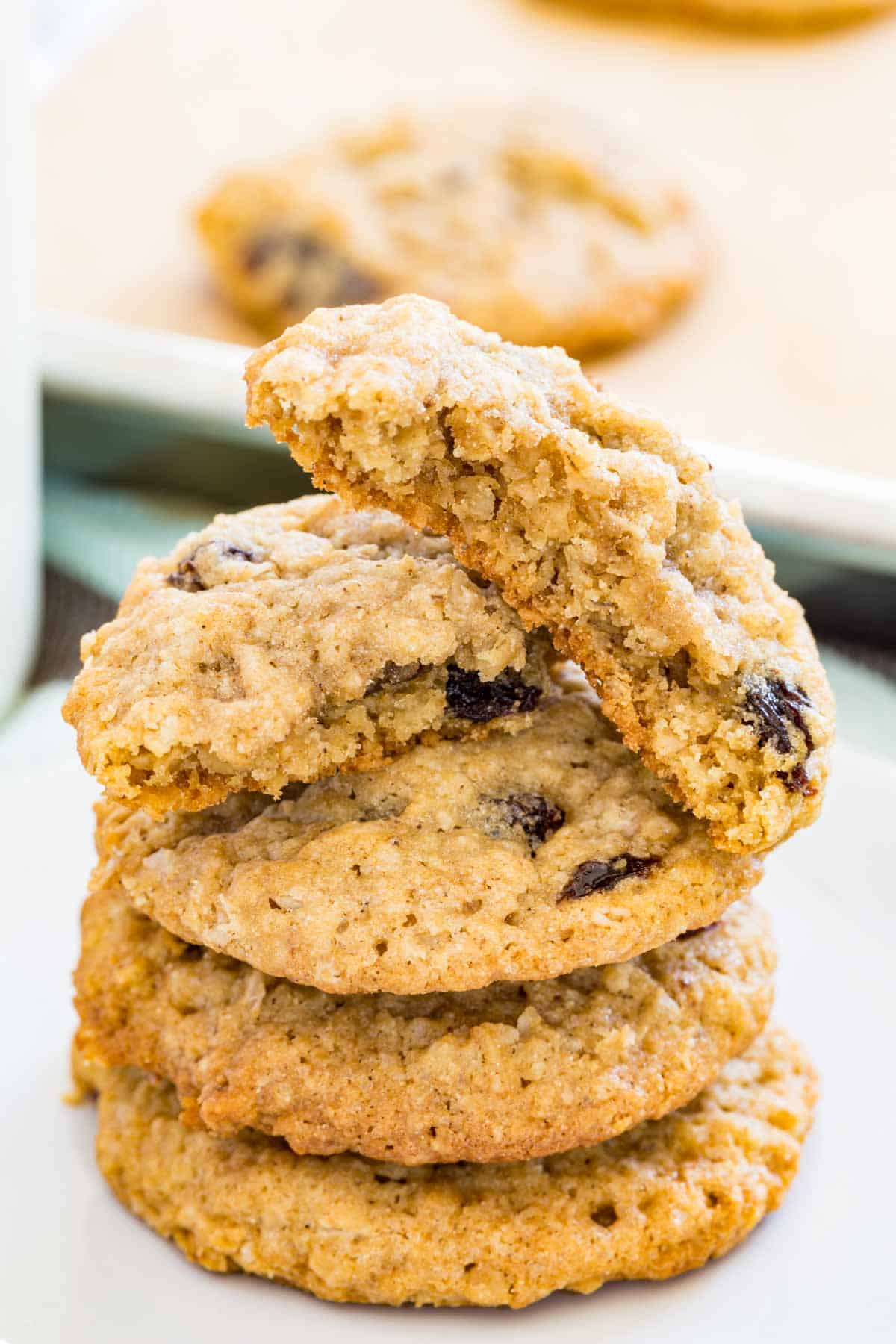 Gluten free oatmeal raisin cookies stacked on a plate, with more cookies on a baking sheet in the background.