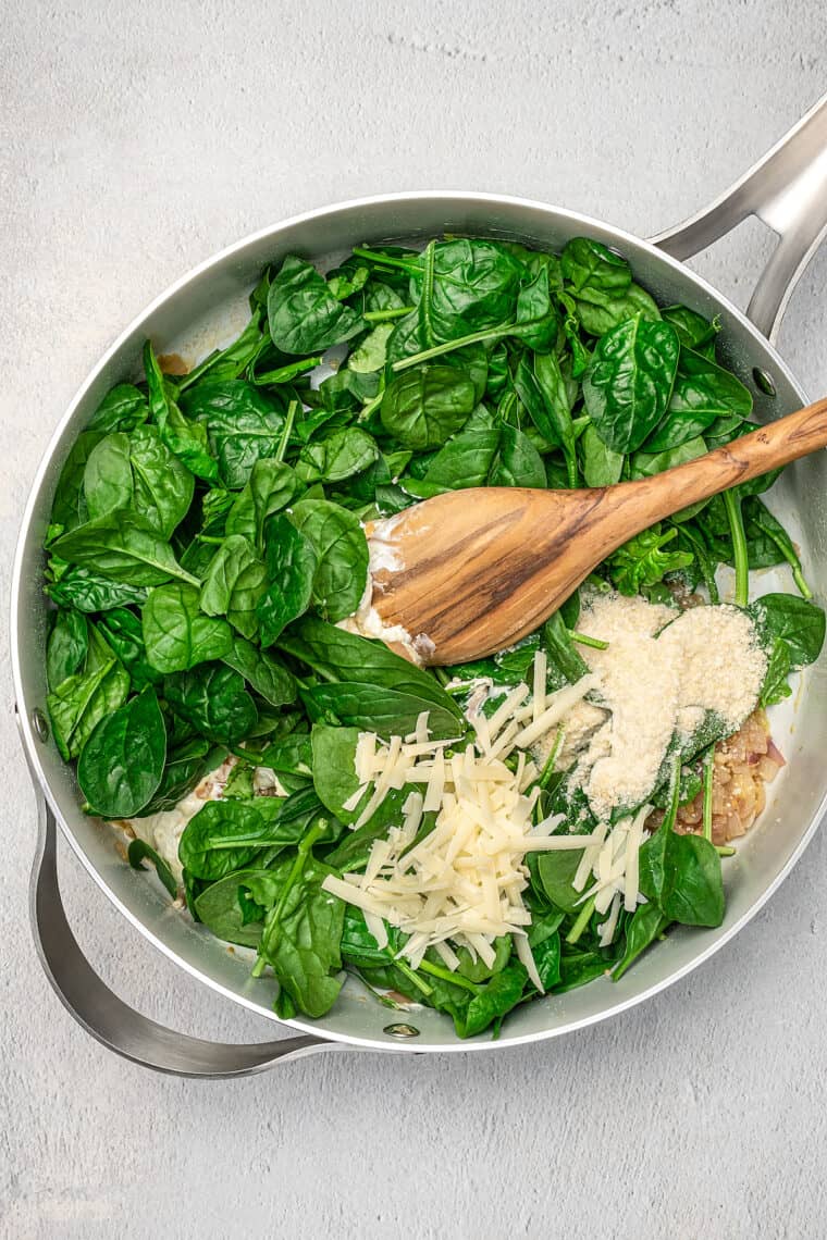 Baby spinach and shredded parmesan is added into a skillet with cream cheese sauce.