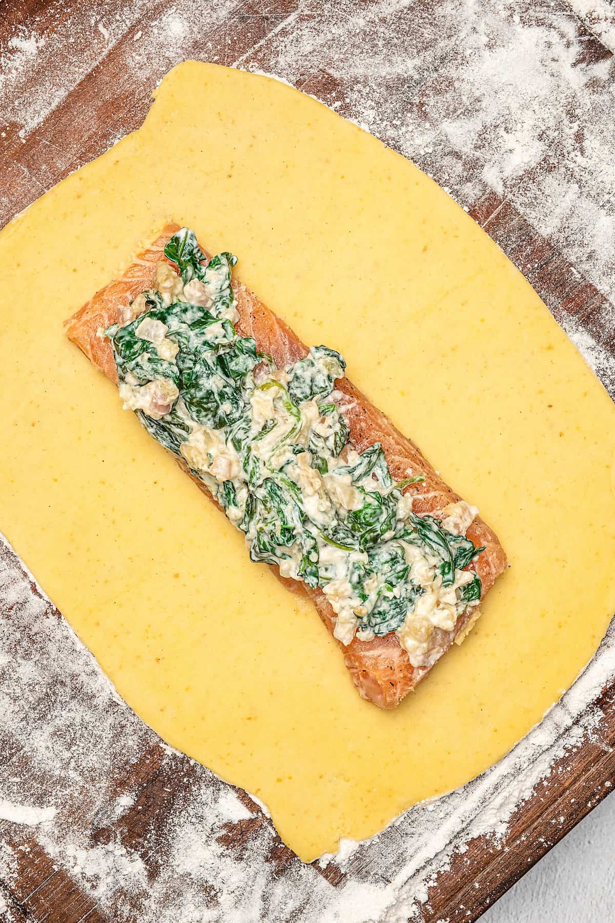 A salmon fillet topped with spinach mixture in the middle of rolled out pastry dough.