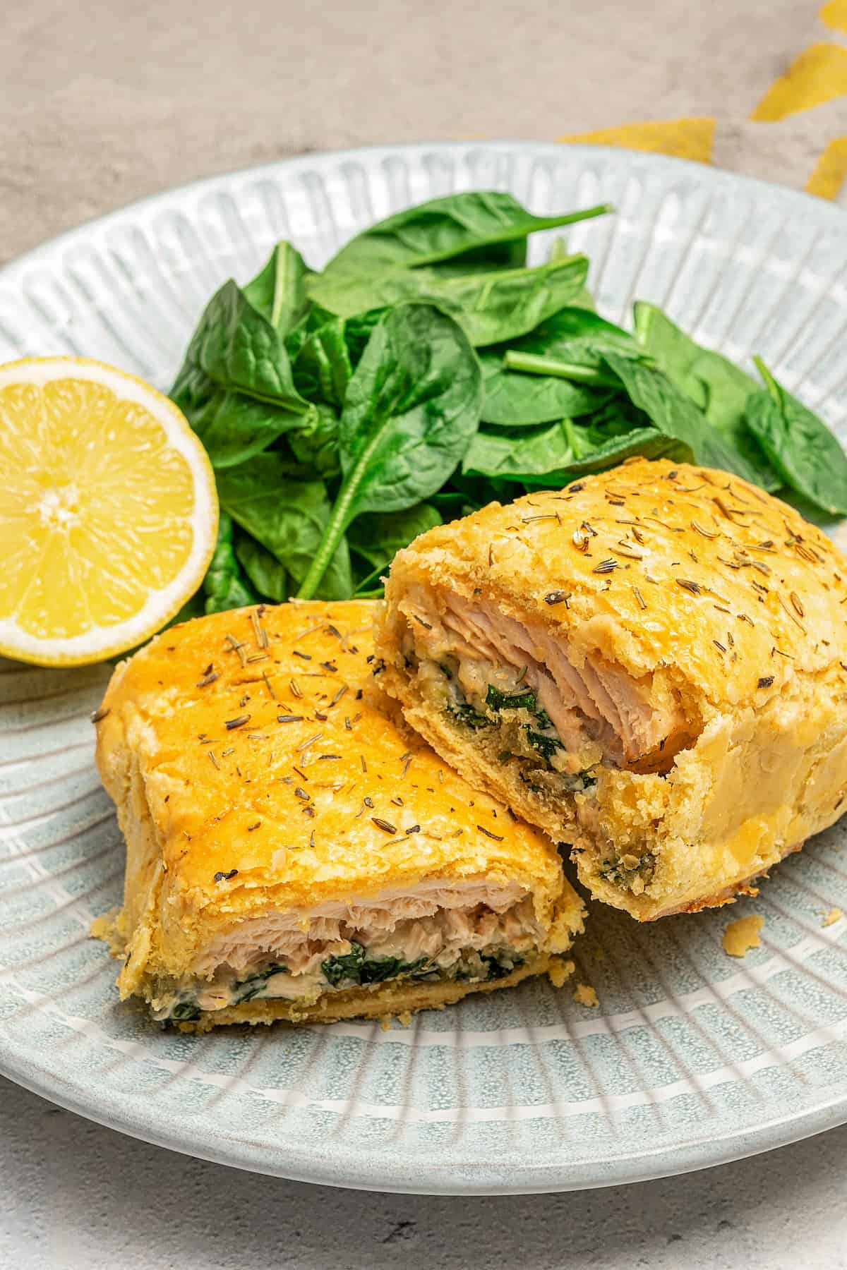Gluten-free Salmon Wellington cut in half on a plate next to half a lemon and fresh spinach leaves and a fork.