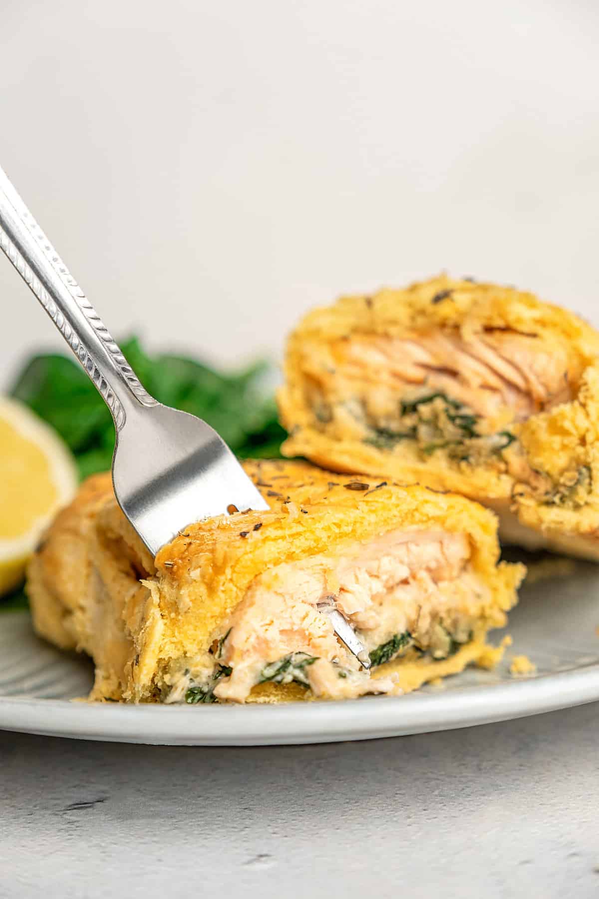 A fork stuck into one half of a gluten-free Salmon Wellington on a plate.