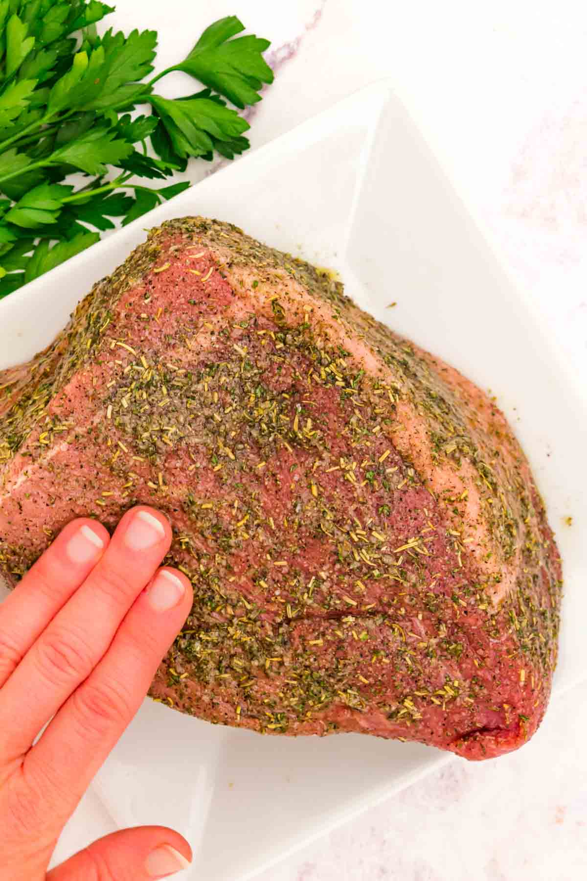A hand pats seasoning all over a bottom round roast.
