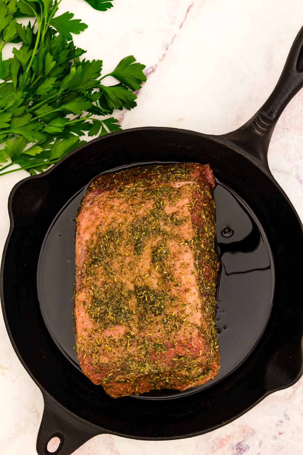 Seasoned, uncooked bottom round roast in a cast iron skillet.